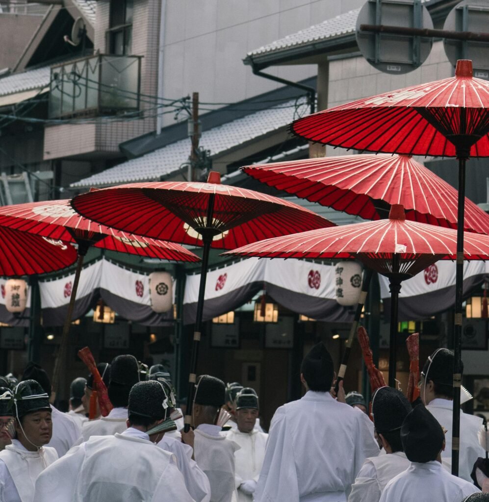 Traditional Japanese street scene with red umbrellas and people in white robes during a festival in Kyoto.