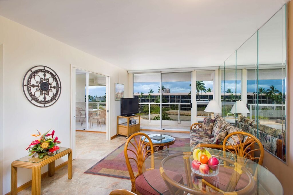 Aston at the Maui Banyan-Bright living room with tropical decor, glass table, and balcony view.