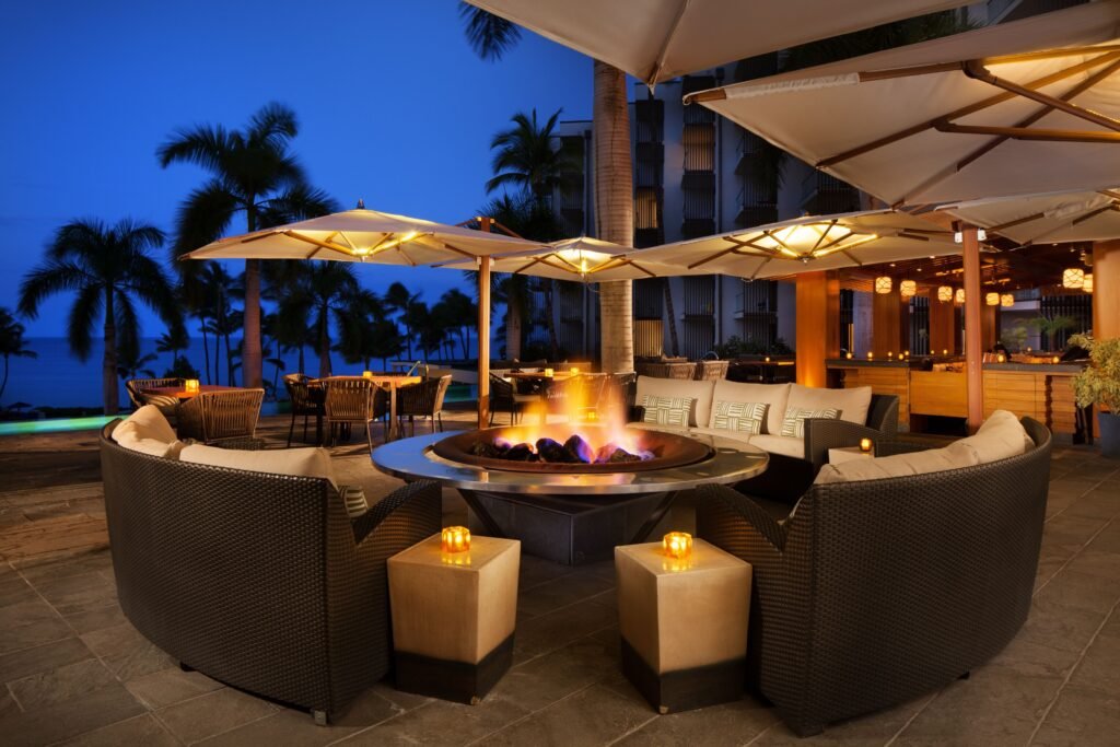 Outdoor lounge with circular fire pit, seating, and umbrellas at dusk. at Andaz Maui at Wailea Resort